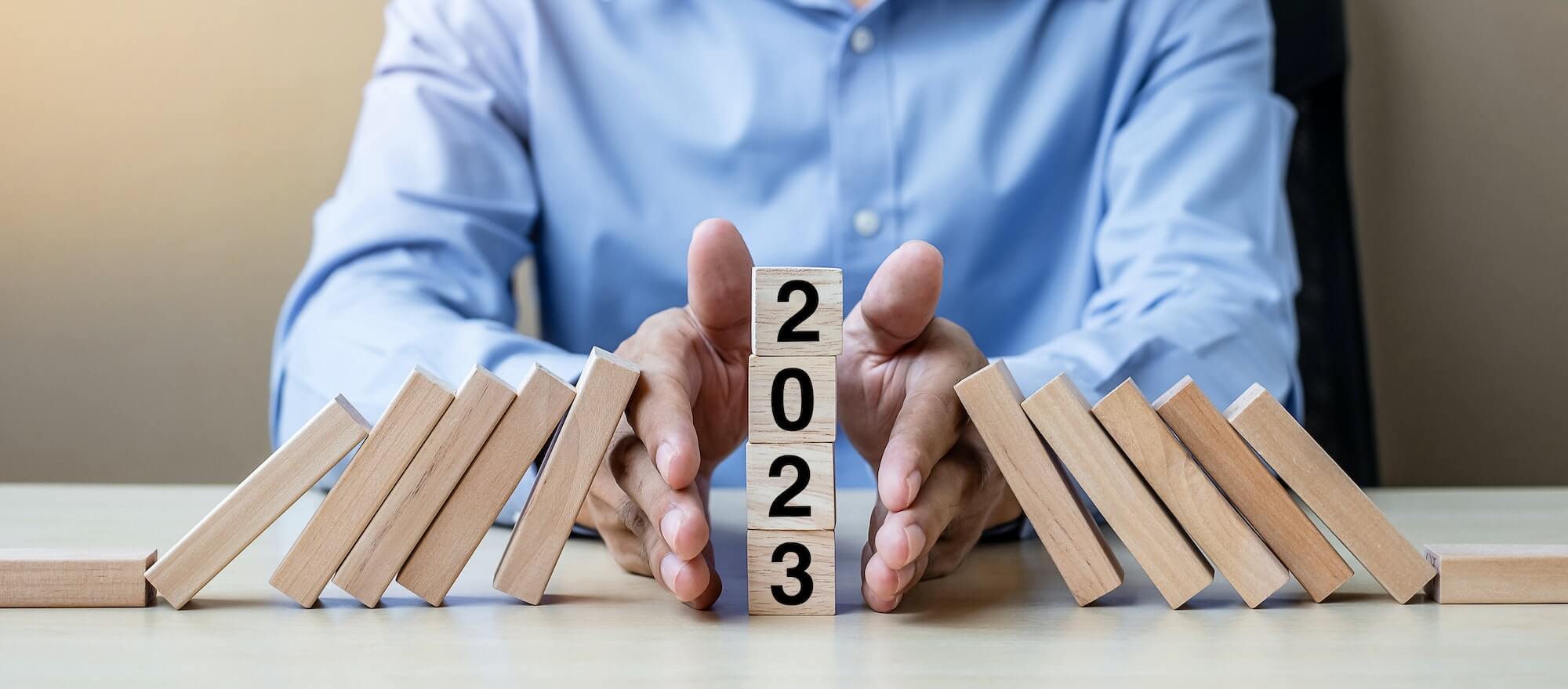 Businessman hand Stopping Falling of 2023 wooden Blocks.