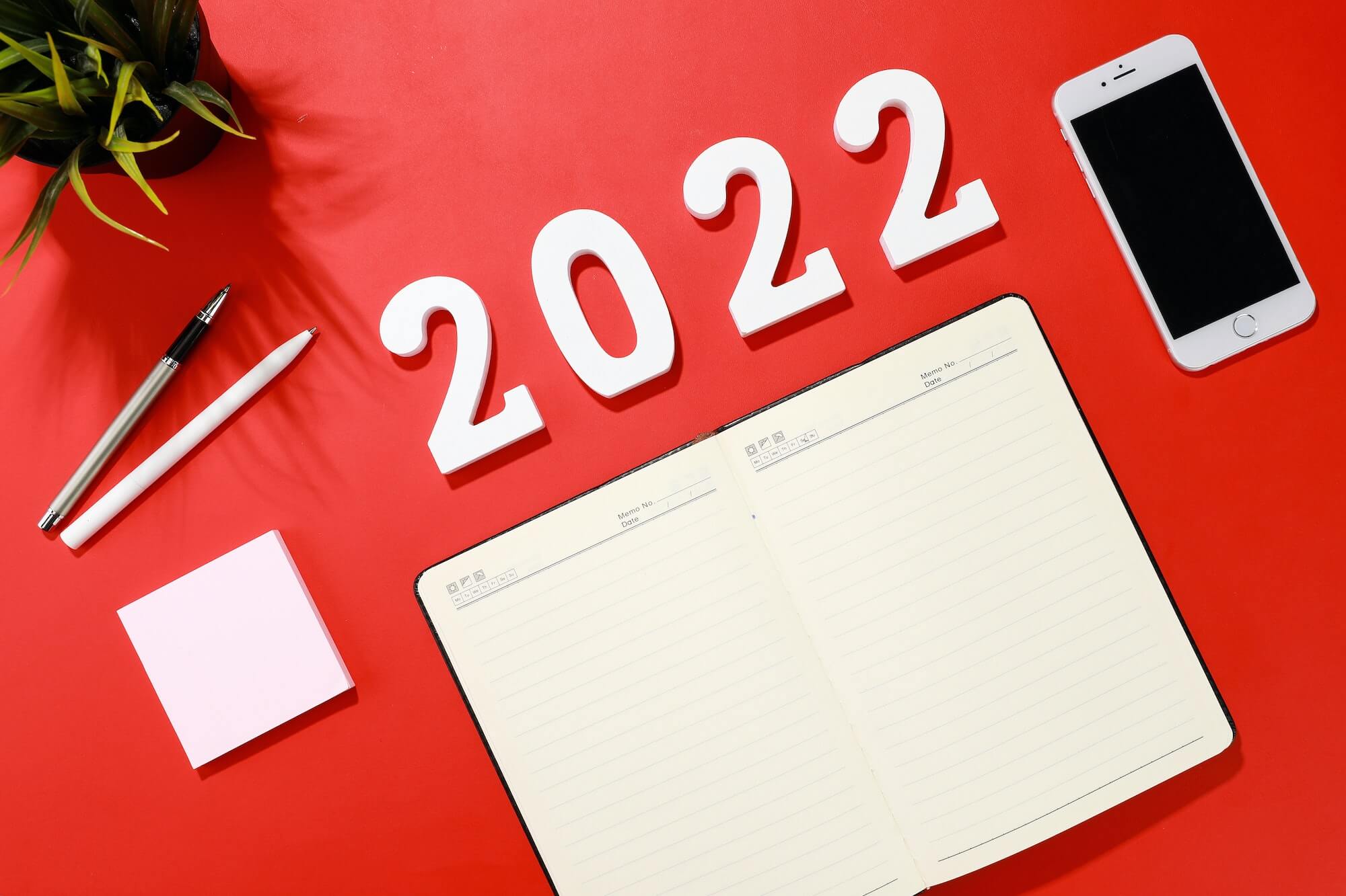 Flat lay shot of a planner, a smartphone, pens and a houseplant on a red background - 2022 goals